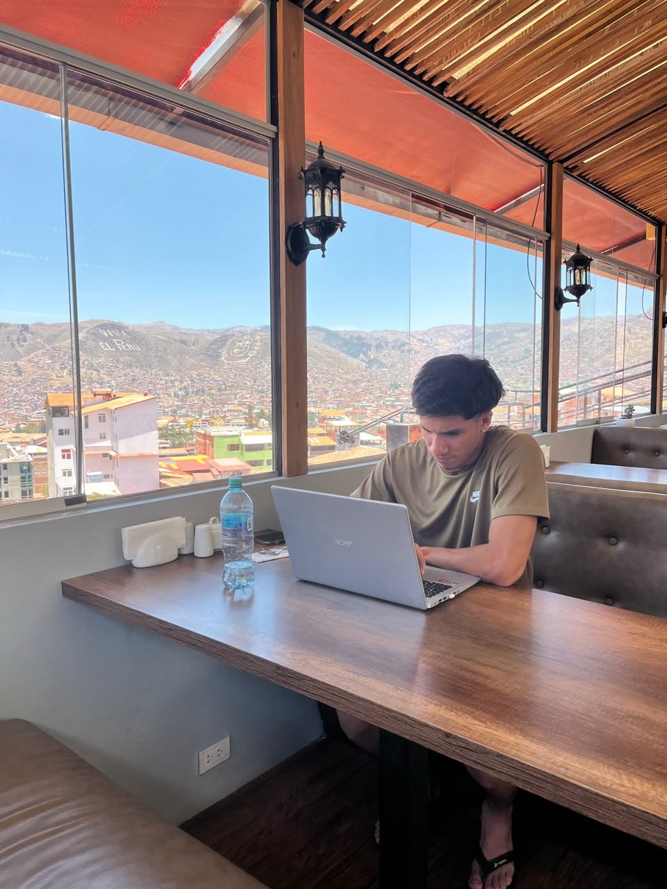 Gabriel trabalhando no notebook em um café com vista para a cidade e as montanhas